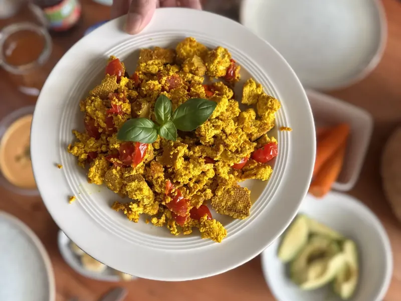 Marvin, der einen Teller Scrambled Tofu über einen gedeckten Tisch hält