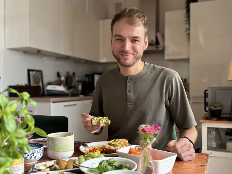 Marvin sitzt am Tisch, hat ein Avocadobrötchen in der Hand und lächelt