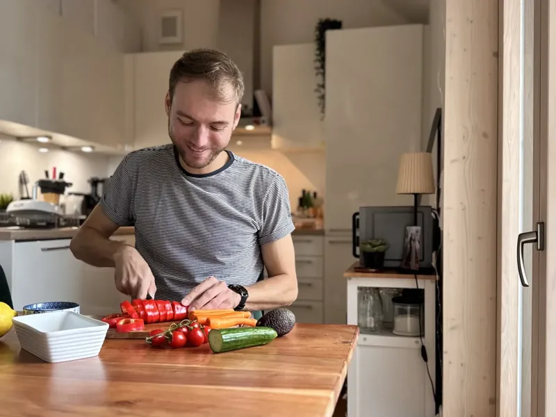 Marvin sitzt lachend am Tisch und schneidet Paprika